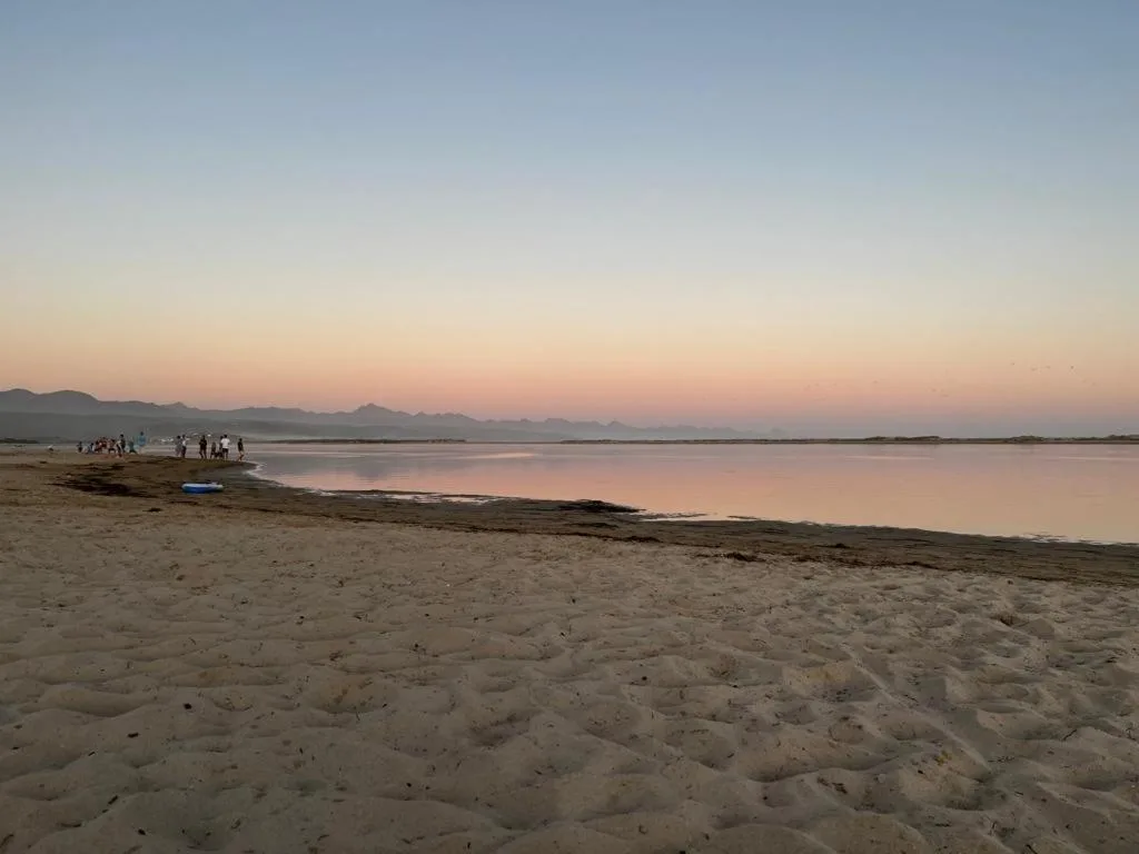 Serene lagoon and mountain vista at dusk from sandy beachfront