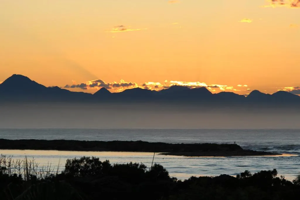 Golden sunset over ocean with mountain silhouettes and breaking waves