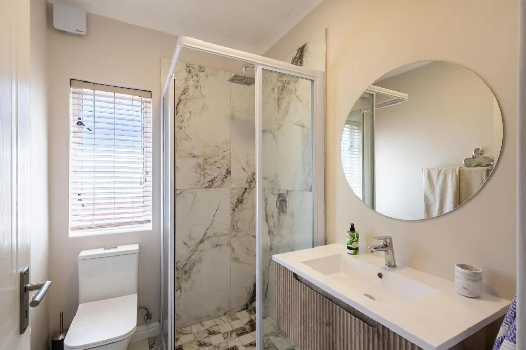 Modern bathroom with marble shower enclosure and round mirror above vanity