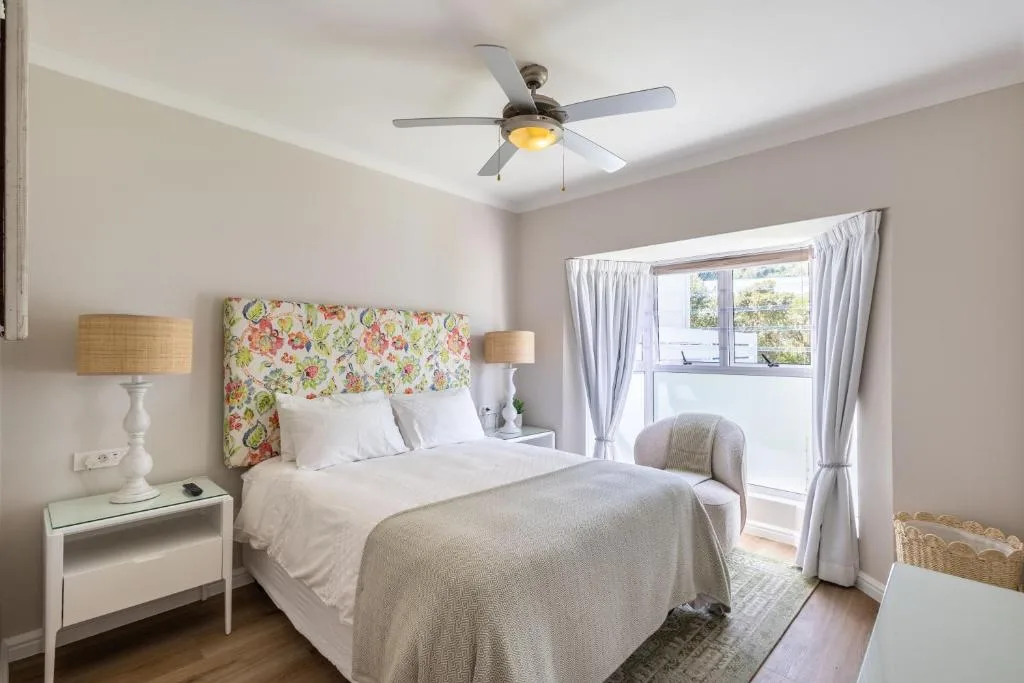 Bright bedroom with floral headboard, white bedding, and garden views through glass doors