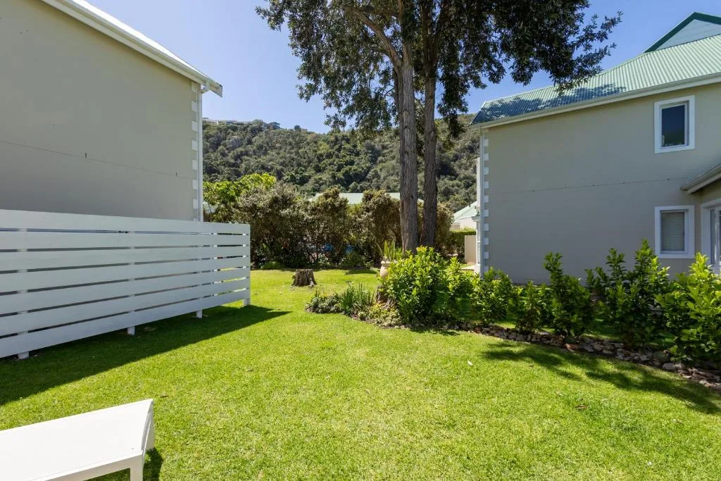Modern home with manicured lawn, white fence, and forested hillside backdrop