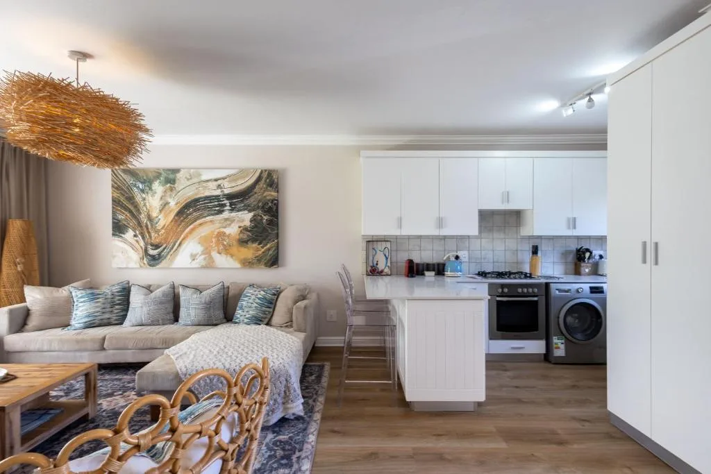 Open-plan living area with cream sofa, kitchen visible beyond, modern fixtures