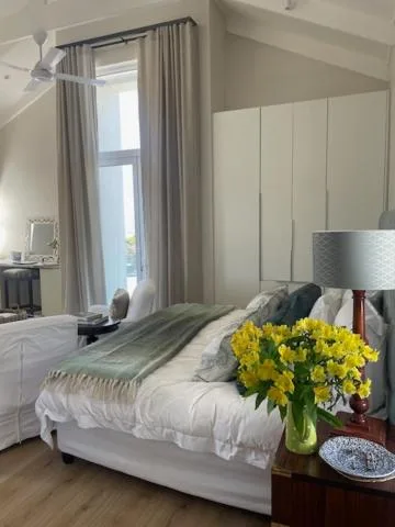 Bright bedroom with white bed, yellow flowers, and ocean view through window