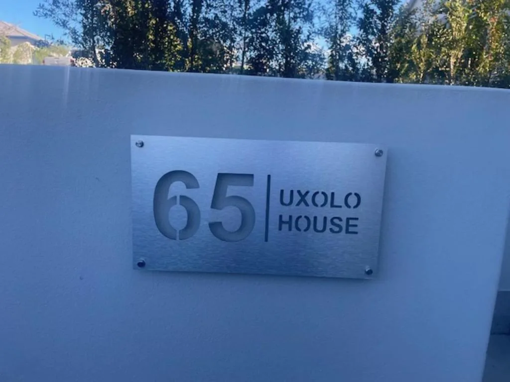 Modern white wall with stainless steel property nameplate reading 65 Uxolo House