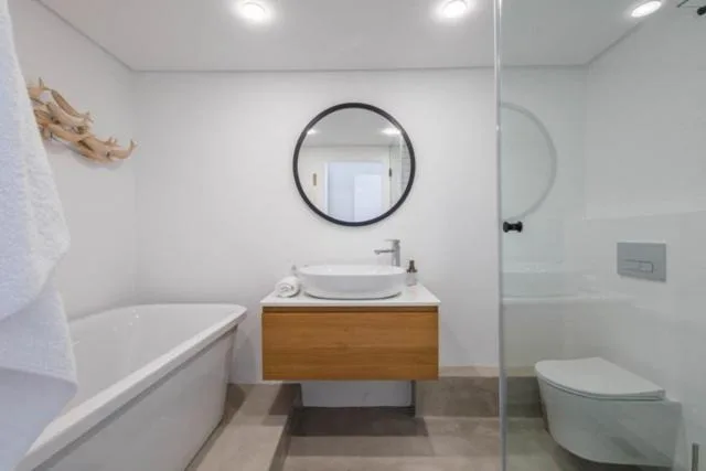 Modern bathroom with freestanding tub, wooden vanity, round mirror, and shower enclosure