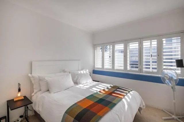 Bright bedroom with white bed, colorful throw blanket, and large windows