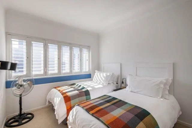Bright bedroom with two single beds, colorful blankets, white shutters