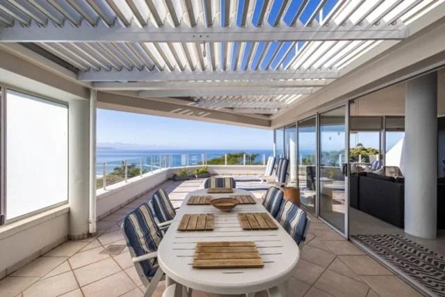 Covered outdoor deck with dining table overlooking ocean and coastal mountains