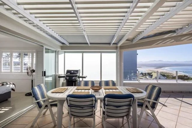 Covered deck with dining table, striped chairs, ocean view