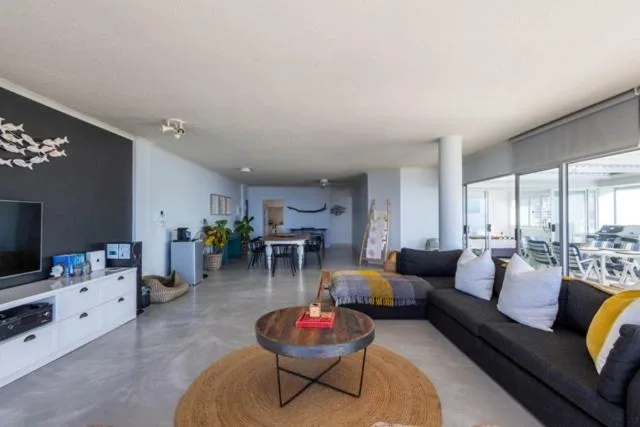 Open-plan lounge with black sofa, TV, and modern furnishings overlooking ocean