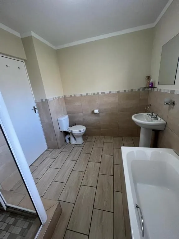 Spacious bathroom with toilet, pedestal sink, and bathtub with shower enclosure