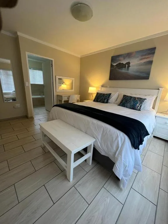 Spacious bedroom with king bed, white bedding, decorative pillows, and coastal artwork