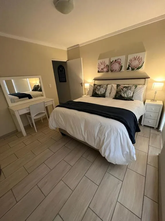 Bright bedroom with white bed, vanity mirror, and botanical wall art