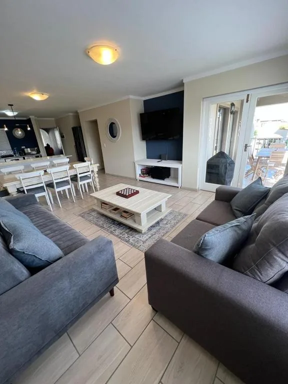 Open-plan lounge with grey sofas, wall-mounted TV, and natural lighting
