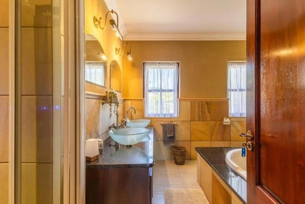 Modern bathroom with dual vessel sinks, gold-tiled walls, and rainfall showerhead