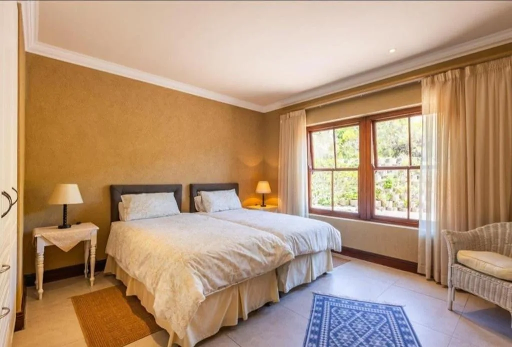 Spacious bedroom with twin beds, warm gold walls, and large windows overlooking gardens