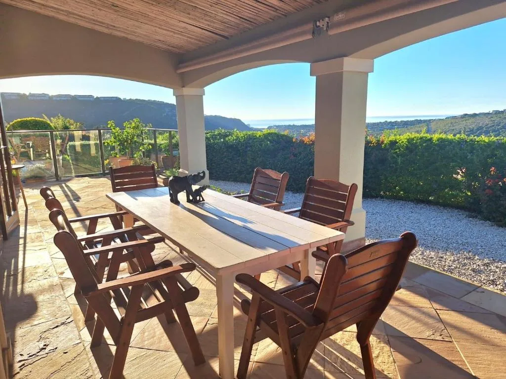 Covered patio with dining table and wooden chairs overlooking lagoon and mountains