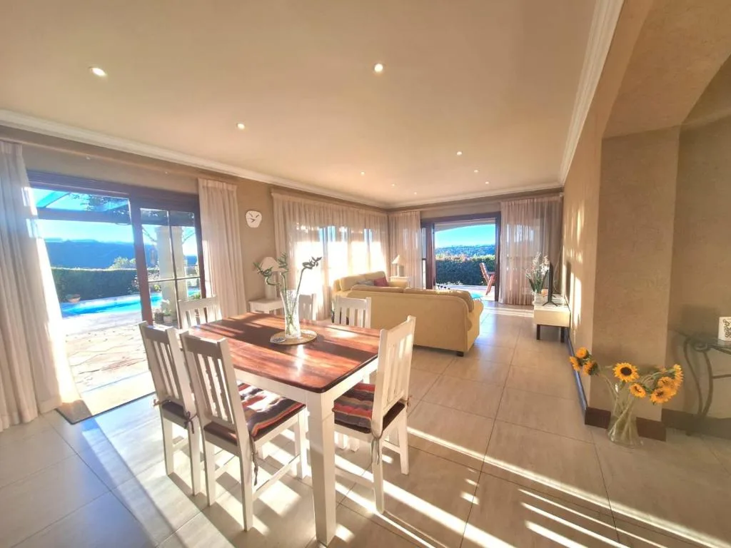 Bright dining area with white chairs and wooden table overlooking ocean views