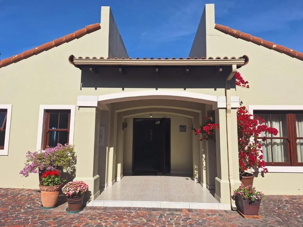 Cream-colored house with curved gable roof and red flowering plants flanking entrance