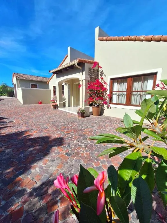 Modern white holiday home with red-tiled driveway and vibrant pink flowering plants