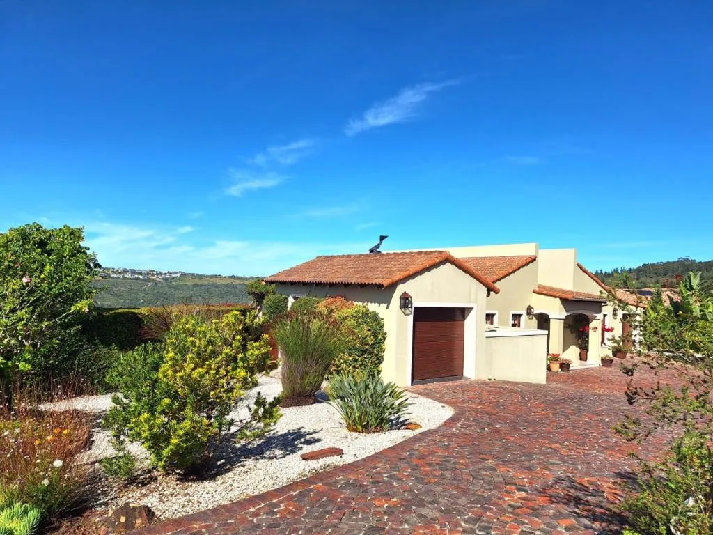 Cream-colored house with terracotta roof and brick driveway in landscaped garden