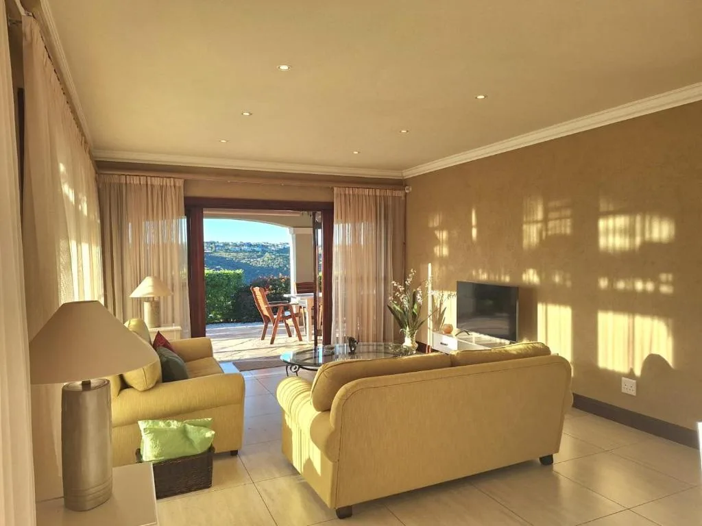 Bright lounge with yellow sofas, TV, and scenic lagoon views through open doors