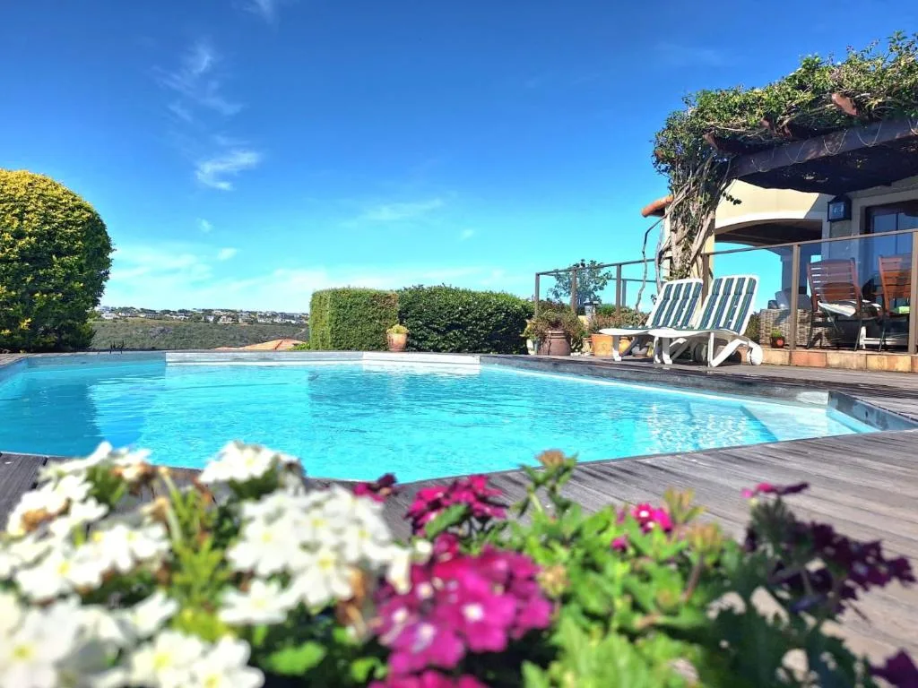 Crystal blue swimming pool with deck, loungers, and scenic hillside views