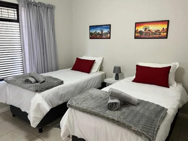 Bright twin bedroom with white bedding, red cushions, and decorative wall art.