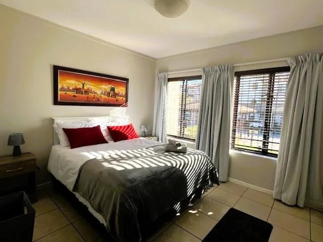 Bright bedroom with queen bed, red pillows, framed artwork, and curtained doors