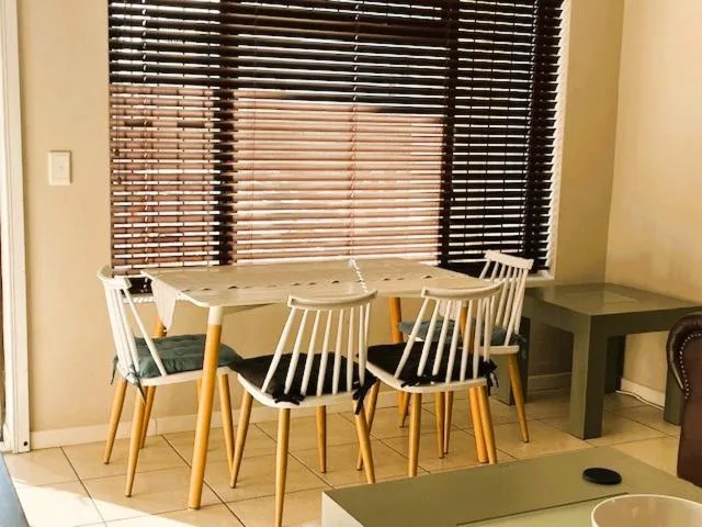 Modern dining table with white chairs near large window with blinds