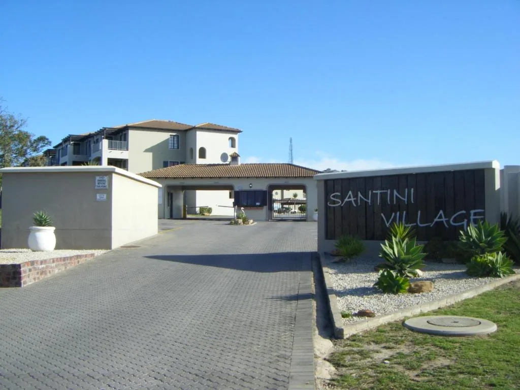 Modern cream and dark building with paved driveway and Santini Village signage
