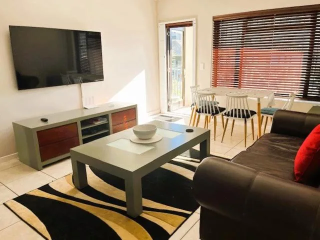 Modern lounge with flat-screen TV, black sofa, and dining area visible