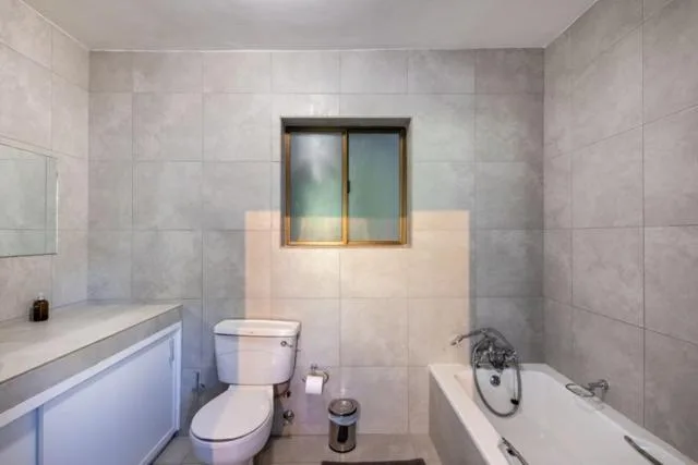 Modern bathroom with white vanity, toilet, bathtub, and gray tile walls