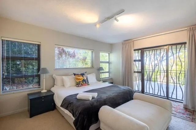 Bright bedroom with queen bed, black nightstand, and garden views through windows