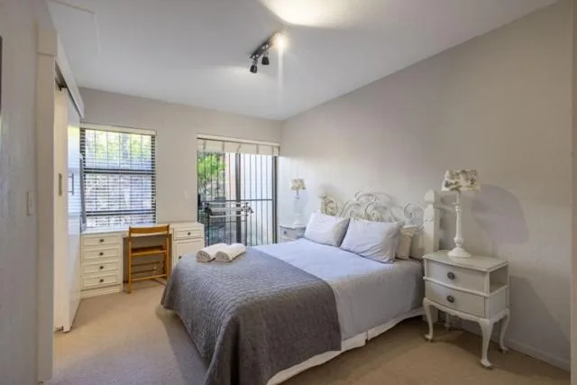 Bright bedroom with queen bed, white nightstand, and garden view doors