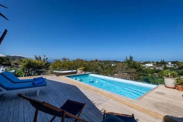 Swimming pool with wooden deck and lounge chairs overlooking coastal hills