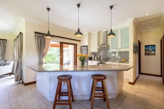 Modern kitchen with island counter, wooden bar stools, pendant lights, and appliances