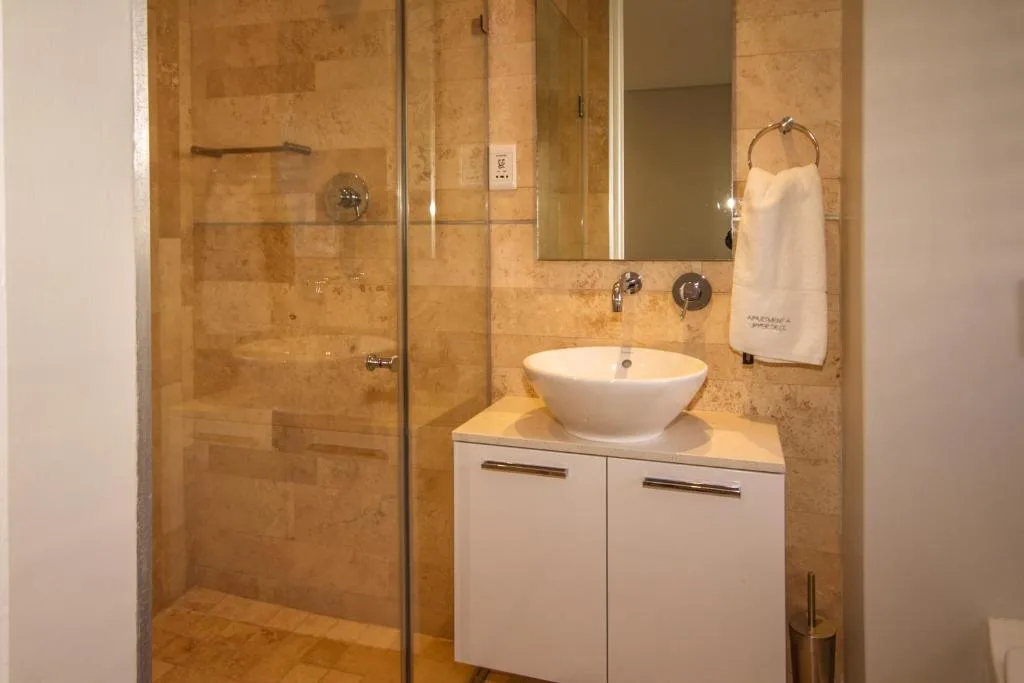 Modern bathroom with vessel sink, travertine tiling, and glass shower enclosure