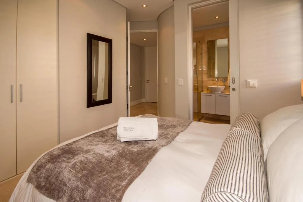 Modern bedroom with twin beds, ensuite bathroom visible, cream décor throughout