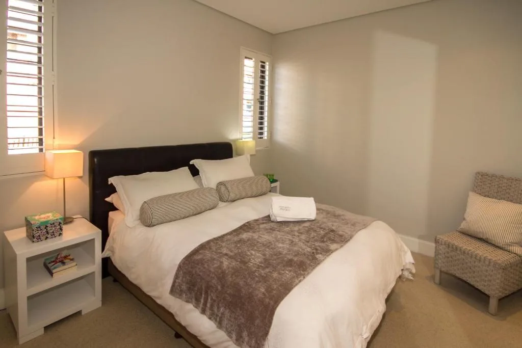 Modern bedroom with dark headboard, white bedding, and natural light from shuttered windows