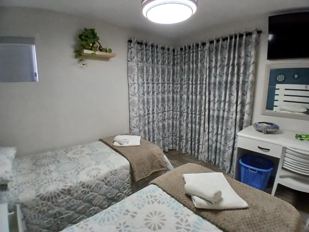 Twin bedroom with patterned curtains, white dresser, and potted plant