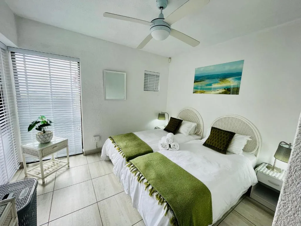 Bright bedroom with two twin beds, white wicker headboards, green accents