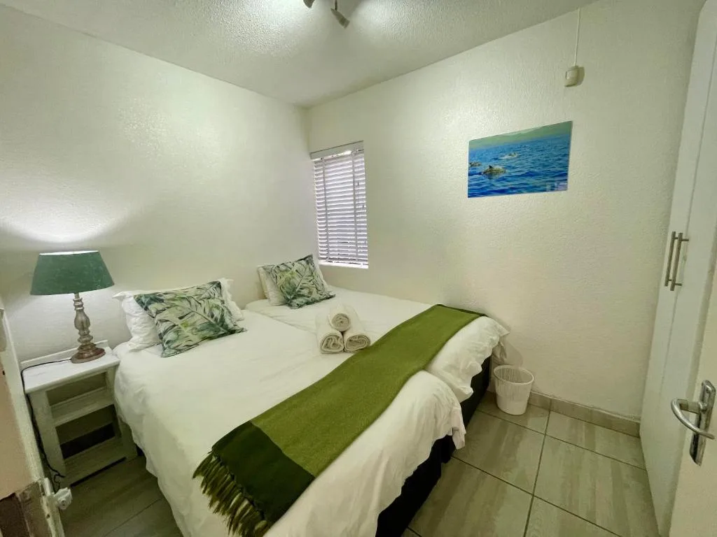 Bright bedroom with twin beds, green accents, and coastal artwork