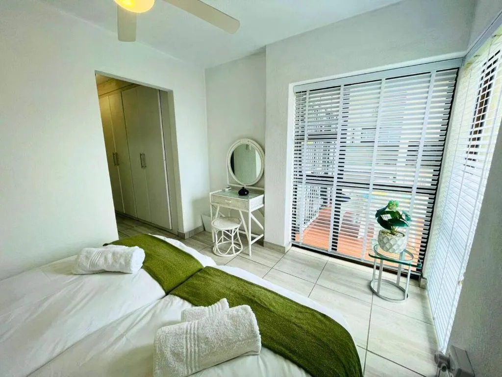 Bright bedroom with bed, green throw, white towels, and shuttered windows
