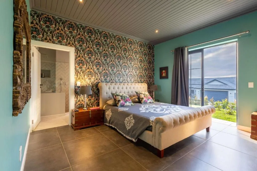 Spacious bedroom with upholstered bed, patterned wallpaper, and ocean views through glass doors