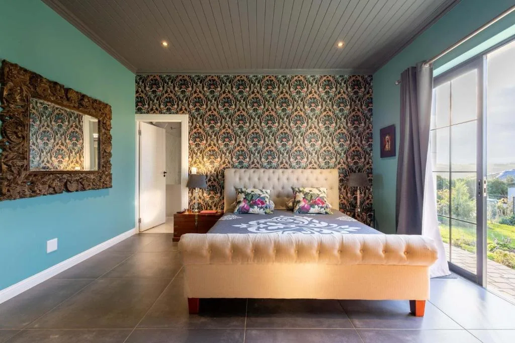 Spacious bedroom with upholstered bed, turquoise walls, patterned wallpaper accent