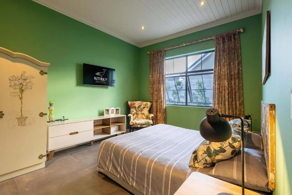 Bright green bedroom with striped bed, armchair, and large windows