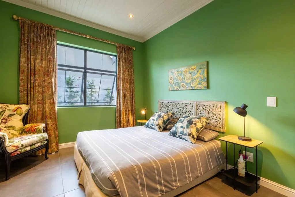 Bright green bedroom with queen bed, patterned headboard, and gold curtains