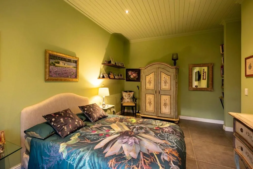 Bright green bedroom with queen bed, floral bedding, and wooden wardrobe
