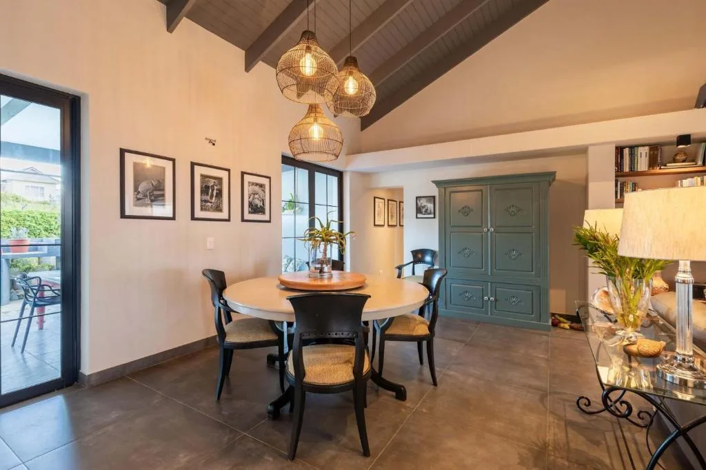Modern dining area with round wooden table and black chairs, pendant lights